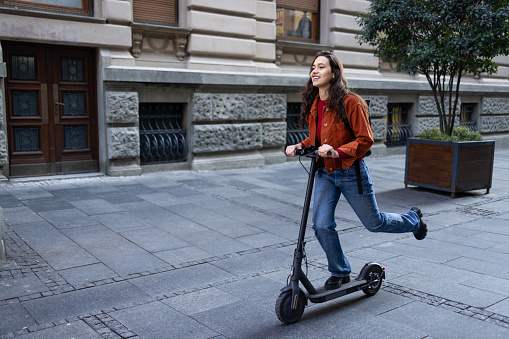 Pretty young woman using her electric scooter for transport from home to work and back