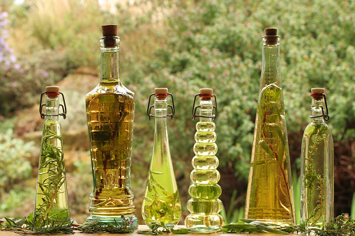 Backlit decorative bottles of herb infused oils and vinegars with the herbs alongside.