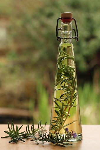 Backlit decorative bottle of rosemary infused oil with the herb alongside.