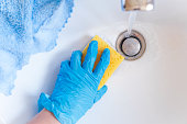 Cleaning the bathroom sink or wash basin. Close up of hand in glove with detergent and microfiber cloth washing polishing washbasin.