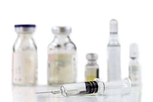 Syringe in front of a surge of vaccines on a white background.