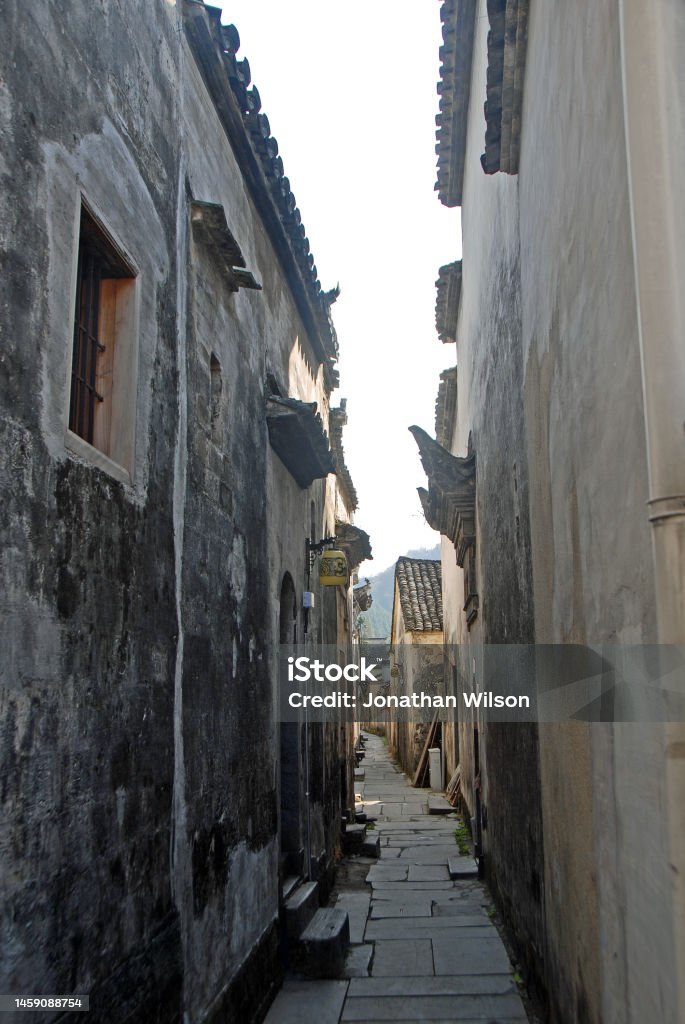 A narrow backstreet in Xidi Ancient Town in Anhui Province, China Xidi Ancient Town in Anhui Province, China. A narrow backstreet in the old town of Xidi with historical buildings, flagstone path and dark walls Alley Stock Photo
