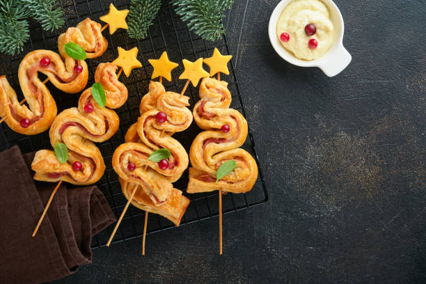 istock Christmas or New Year appetizer. Christmas tree shape puff pastry buns with cheese and ham. Group of Christmas tree shapes on wooden board. Festive idea for Christmas or New Year dinner. Top view. 1459089016