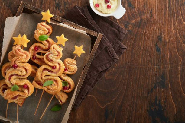 istock Christmas or New Year appetizer. Christmas tree shape puff pastry buns with cheese and ham. Group of Christmas tree shapes on wooden board. Festive idea for Christmas or New Year dinner. Top view. 1459089173