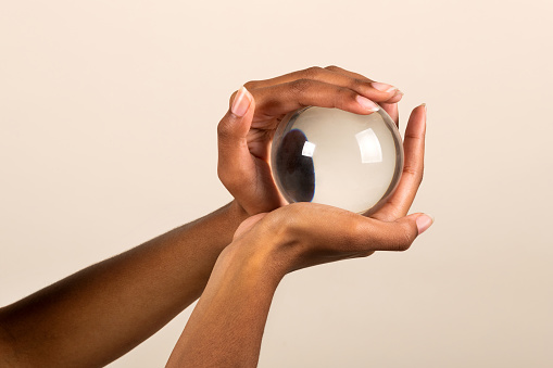 Closeup of crop anonymous African American female holding transparent glass sphere in hands on pink background