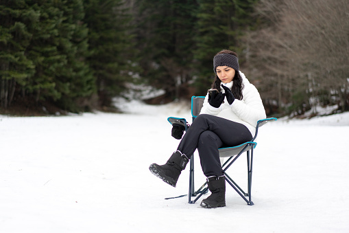 a woman sitting on camping chair in snowy weather hanging out with smartphone