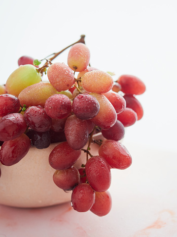 bunch of wet fresh grapes in a pink bowl close-up view. Freshly washed with water droplets