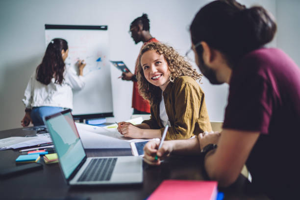 istock Cheerful employees having nice conversation sitting at table while other diverse office workers using board to discuss project in workplace 1459106403