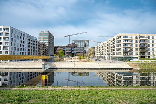 modern residential houses reflecting in Berlin river, new district under construction with cranes in background