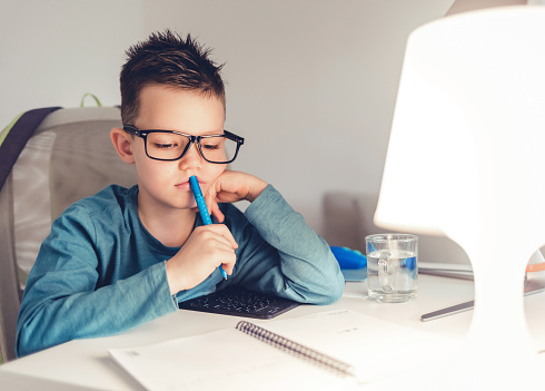 Boy doing homework in his room, seating on the chair and work on the desk.