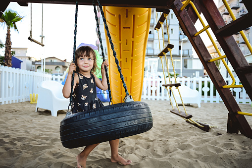 little girl in a summer dress having fun on chain swing.