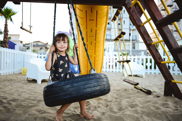 маленькая девочка в летнем платье развлекается на цепных качелях. - tire swing стоковые фото и изображения