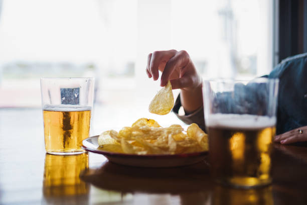 Shot of a girl taking a chip from a plate. There is also beer glasses next to it.