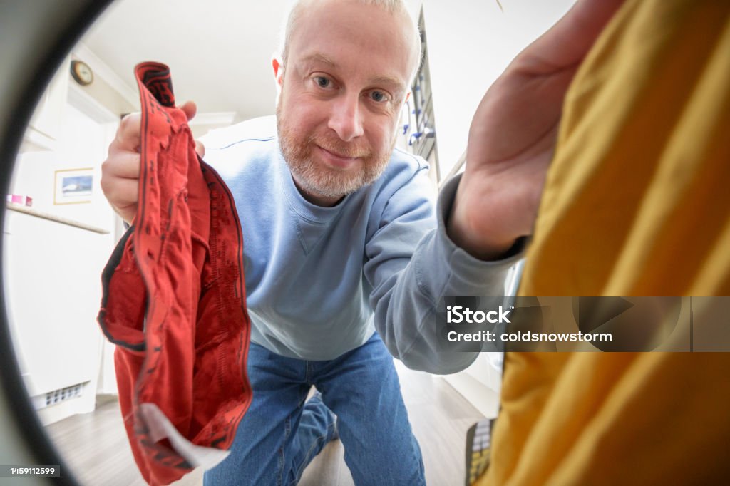 Man loading his washing machine with dirty laundry, POV shot Wide angle color image depicting a mid adult male putting dirty clothes in the washing machine. The camera is positioned inside the washing machine, looking out at the man performing this domestic chore. Personal Perspective Stock Photo