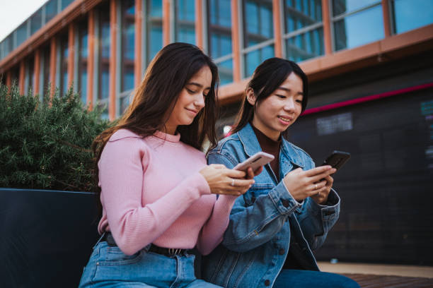 istock Two smiling girls using their smart phones 1459113367
