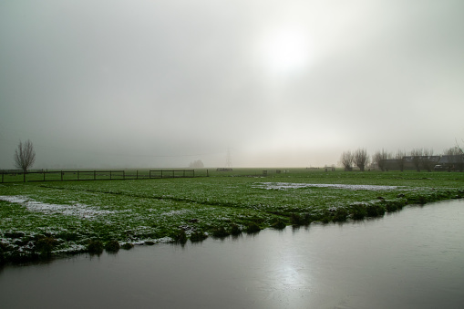 typical dutch country landscape with fog above the meadow in winter with frozen ditch. Woerden, The Netherlands