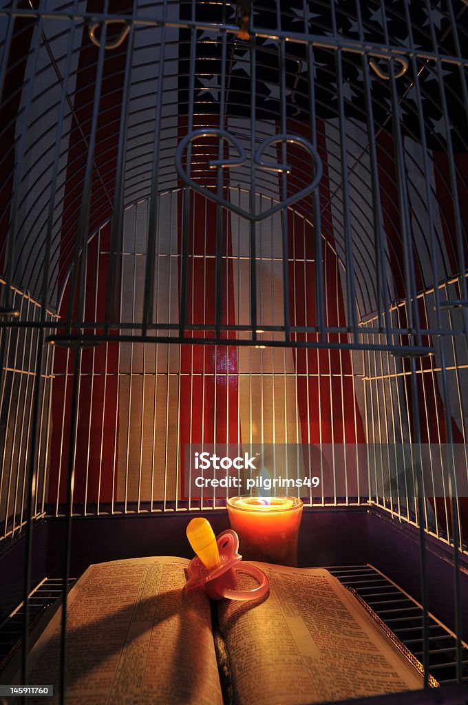 American Evangelicalism An open Bible in a birdcage with a baby pacifier, candle, and American flag. American Flag Stock Photo