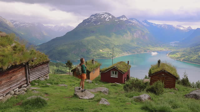 Rear view of a woman contemplating the scenic mountain valley with old wooden houses in Norway