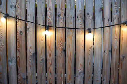 Glowing light bulbs hanging on natural wooden wall made of vertical planks for product advertising billboard concept or website design