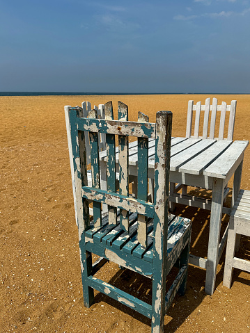 Stock photo showing the golden sands of Mount Lavinia Beach, Colombo, Sri Lanka with al fresco dining area of rustic white painted tables and chairs background of blue sea and sky.