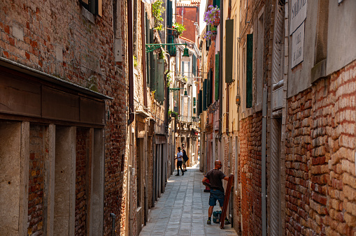 People in a brick alleyway in the city of Venice during the summer