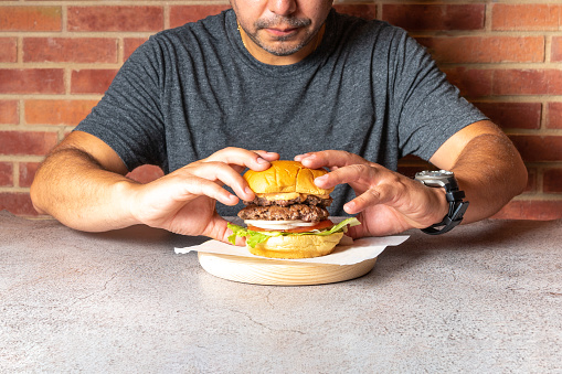 Unrecognizable man picking up a typical American hamburger with both hands to start eating. High quality photo