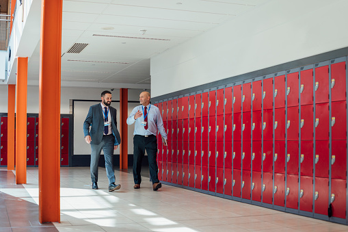 A wide angle view of two male teachers who are walking from one class to another in the high school that they work at in The North East of England.