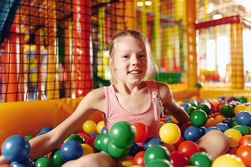 Happy little girl playing in amusement park balls pool. Kids cheering and playing with plastic colourful balls. Children throwing balls high. Playing with balls: activities for children