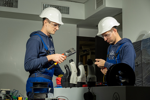 Technicians work with pliers in workshop and install cables into plugs to charge EV on stations. Electricians check work of charging connectors