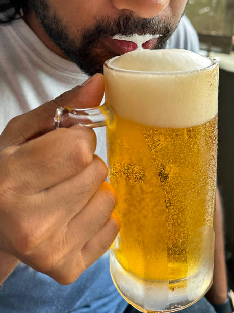 imagem de quadro completo do homem indiano bebendo cerveja de tanque de vidro com bolhas efervescentes formando cabeça espumante de espuma em cima de cerveja, bigode espumoso, foco em primeiro plano - beer glass mustache beer color image - fotografias e filmes do acervo