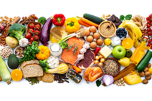 Overhead view of a large group of all sort of food for a well balanced and healthy diet of proteins, dietary fiber, carbohydrates, vitamins and minerals arranged side by side on white background. The composition includes fruits, vegetables, fish, raw meat, beans, seeds and nuts, pasta, cooking oil, spices and dairy products. High resolution 42Mp studio digital capture taken with SONY A7rII and Zeiss Batis 40mm F2.0 CF lens