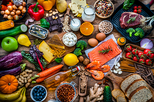 Overhead view of a large group of all sort of food for a well balanced and healthy diet of proteins, dietary fiber, carbohydrates, vitamins and minerals. The composition includes fruits, vegetables, fish, raw meat, beans, seeds and nuts, pasta, cooking oil, spices and dairy products. High resolution 42Mp studio digital capture taken with SONY A7rII and Zeiss Batis 40mm F2.0 CF lens