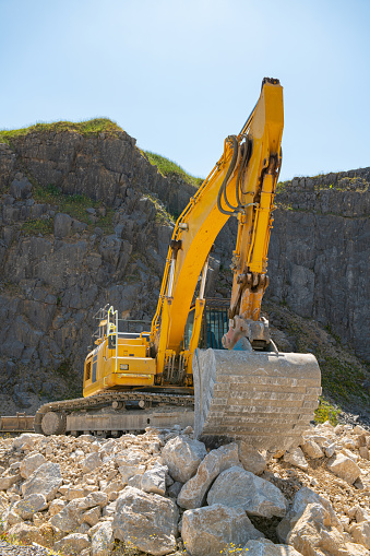A yellow excavator in a quarry in summertime