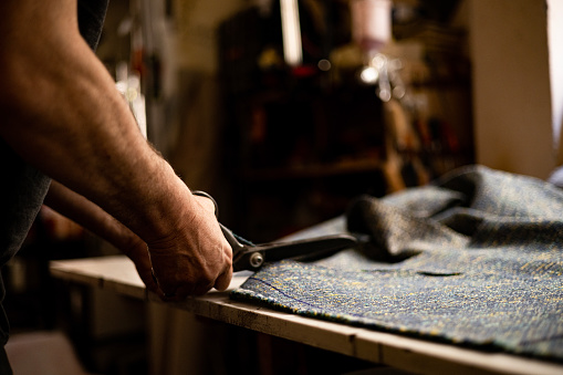 Close up of unrecognizable male carpenter cutting fabric while working in a workshop.