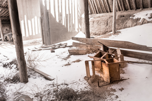 Interior of abandoned potato bunker, San Luis Valley, Colorado, on winter day. Sunlight through slats of roof casing shadows on wall. Snow on floor. Artifacts on floor with snow.