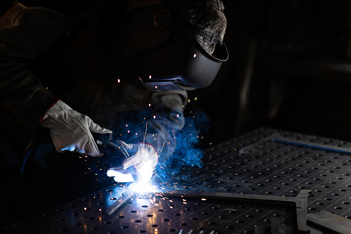 Steel worker welding metal while working in a workshop.