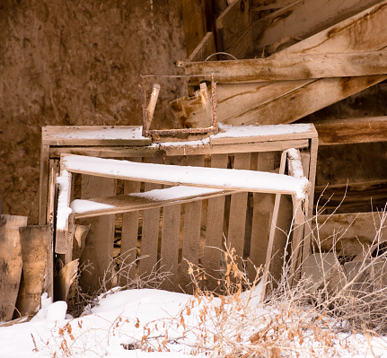 Overgrown nterior of abandoned potato bunker, San Luis Valley, Colorado, on winter day. Heavy beams. Snow on floor. Wooden tools and artifacts on floor with snow.