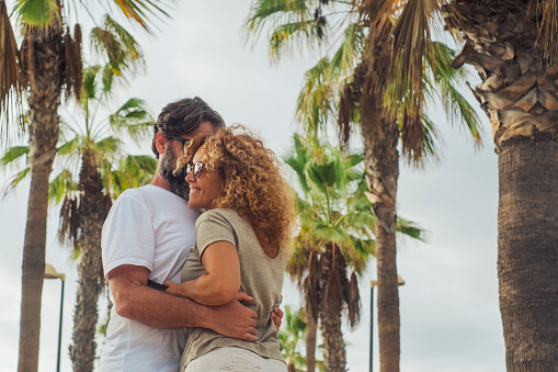 Adult couple man and woman enjoying relationship hugging with happiness outdoor in a palms street during summer holiday travel vacation. Outdoor leisure activity people in love and friendship smiling