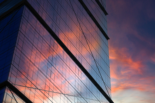 Modern business building with glass facade with sunset and sky reflection.