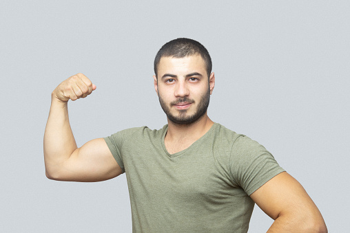 Portrait of a young man showing his bicep over gray background.