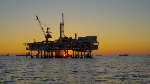 silhouette große industrielle gas- und öl-offshore-bohrinsel in ruhigen gewässern mit untergehender sonne an einem klaren abend in der abenddämmerung mit catalina island im fernen hintergrund - oil rig sea oil storm stock-fotos und bilder