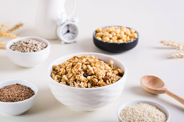 granola assada em uma tigela e sementes diferentes em tigelas sobre a mesa. café da manhã saudável. - granola cereal breakfast stack - fotografias e filmes do acervo