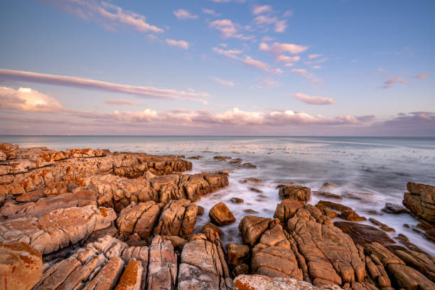 Crashing Waves on the Rocky Shoreline of Fish Hoek with a Vibrant Sunset Over False Bay on the Cape Peninsula Outside Cape Town, South Africa stock photo