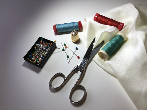 Scissors, threads, pins and fabric on grey background