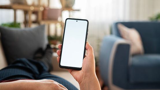 Woman using phone with white screen while lying on sofa at home , mock up screen