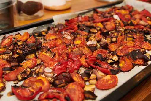 High angle close-up of roasted various fresh vegetable slices in baking sheet on table in kitchen
