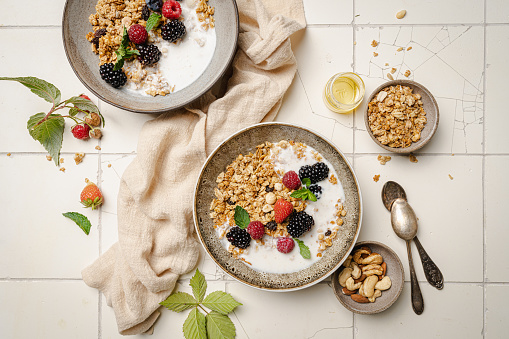 Bowl of homemade granola with yogurt and fresh berries on white background from top view