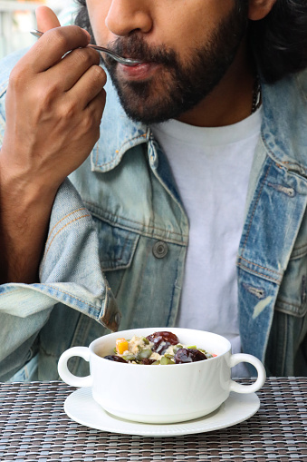 Stock photo showing close-up view of some freshly made muesli in a white ceramic bowl with handles on a plate. Eating a bowl of oats is believed to have important long-term health benefits, helping to prevent heart disease.