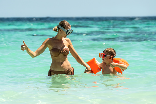 Photo of happy mother and her little son snorkeling on tropical beach, having fun together. Hobby. Water sports concept. Summer. Tourism.