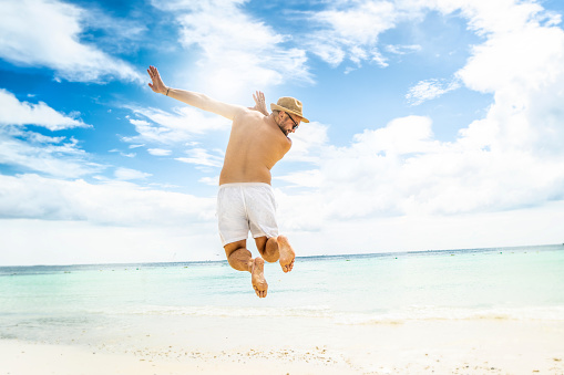 Happy man jumping over sea. Sand beach and blue water. Summer vacation. Tropical island.